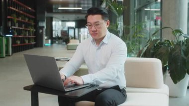 Gibi. Bilgisayarda çalışan mutlu genç işadamı kameraya bakıp olumlu bir işaret veriyor. Modern ofis lobisinde oturan olumlu bir geri bildirim gibi. İş insanları