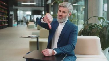 Hoşlanmamak. Takım elbiseli üzgün işadamı ofis lobisinde oturmuş işaret dilini gösteriyor hoşnutsuzluğunu, memnuniyetsizliğini ve kötü işini dile getiriyor. Otel odasında ciddi bir olgun adam var..