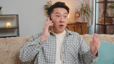Gülümseyen genç Çinli bir adam evdeki kanepede oturan arkadaşlarıyla eğlenceli telefon konuşmaları yapıyor. Mutlu, heyecanlı Orta Doğulu satıcı içeride cep telefonu konuşmaktan hoşlanıyor..