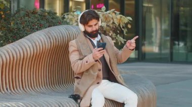Kablosuz kulaklıklarıyla dans eden, akıllı telefon dansında enerjik disko müziği dinleyen mutlu, neşeli Hintli genç işadamı. Lübnanlı sakallı adam şehir merkezindeki bankta oturuyor.