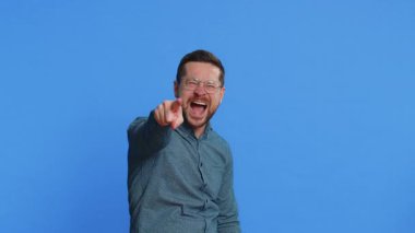 Beyaz, orta yaşlı bir adam kamerayı işaret ediyor, yüksek sesle gülüyor, komik görünüşle dalga geçiyor, komik fıkra anlatıyor, zorbalık ediyor, taciz ediyor. Genç yetişkin adam mavi arka planda izole edilmiş