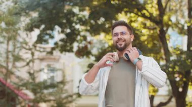 Kafkasyalı genç adam kablosuz kulaklık takıyor, açık havada akıllı telefondan en sevilen enerjik müziği dinliyor. Gülümseyen turist şehir sokağının yanından geçiyor. Kasaba yaşam tarzları.