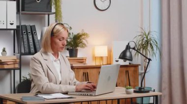 Kulaklık takmış kendine güvenen Kafkasyalı yetişkin bir iş kadını bilgisayarla ofis masasında konuşuyor. Kadın danışmanın internet danışmanı var, müşterilere yardım ediyor, müşteri desteği şikayetlerle.