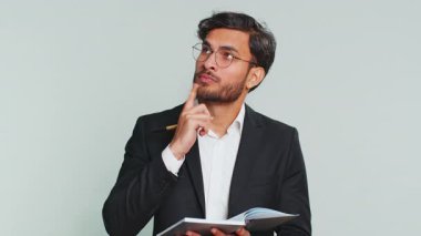 Düşünceli gazeteci Hintli işadamı notlar alıyor, not defterine kalemle düşünceler yazıyor, liste yapmak için, iyi fikir. Erkek Arap erkek avukat. Gri arka planda tek başına.