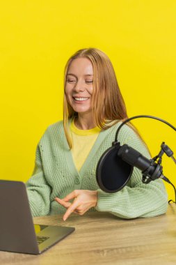 Mutlu heyecanlı kadın blogcu masa kaydı podcast, atölye çalışması, webinar. Yetişkin kız etkileyicisi mikrofon ve dizüstü bilgisayara konuşuyor, video görüşmesi yapıyor, sarı arka planda tartışıyorlar..