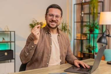 Genç işadamı serbest hisse senedi tüccarı elinde tuttuğu parayla online ticaret operasyonlarını izledikten sonra bitcoin gösteriyor. Zenginliği artırmak, finansal refahı arttırmak. Ofis masasında dizüstü bilgisayarı olan adam..