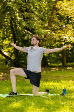 Sportif formda bir adam parkta yoga yaparken spor minderinde nefes egzersizi yapıyor. Ellerinizi kaldırın. Koşucu dışarıda egzersiz yapmaktan hoşlanıyor. Aktif sporcu motivasyonu. Aktif sporcu sağlıklı yaşam tarzı.