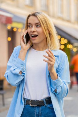 Beyaz kadın turist uzaktan iletişim kuruyor arkadaşlarıyla akıllı telefondan konuşuyor şehir caddesinde beklenmedik bir şekilde iyi haber dedikoduları yapıyor. Şehir yaşam tarzları açık havada