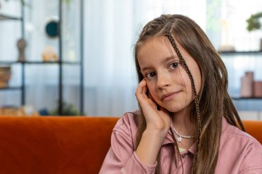 Mutlu gülümseyen genç kız çocuğunun portresi rahat koltukta oturup evdeki oturma odasındaki kameraya bakıyor. Kahverengi uzun saçlı, tatlı, genç bir kız öğrenci. Yaşam Tarzları.