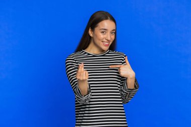 Bana para ver lütfen. Kafkasyalı genç bir kadının parmaklarını ovuşturması borçlarını ödemek için nakit para talep ettiğini gösteriyor. Borç al, alışveriş yap, yatırım için yalvar. Stüdyo mavi arka planda izole edilmiş kız