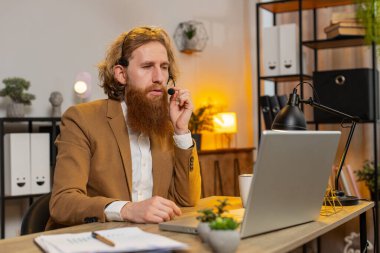 Kafkas işadamı kulaklık takıyor, serbest çalışan, çağrı merkezi ya da destek operatörü yardım hattı, müşteri ya da iş arkadaşı iletişim desteği ile konuşuyor. Kızıl saçlı adam ofis masasında oturuyor..