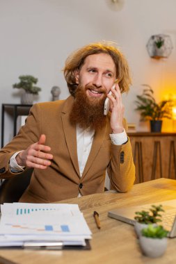 Genç işadamı ofis masasında oturuyor cep telefonuyla müşteriye cevap veriyor, akıllı telefon kullanıyor. Sohbet. Uzaktan kumandalı internet işinde çalışan beyaz bir adam konuşuyor. Dikey