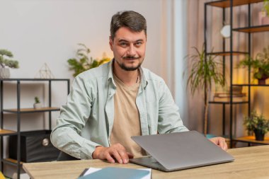 Oturma odasındaki işi bitirdikten sonra masadaki bilgisayarı kapatan genç adam. Happy Kafkasyalı serbest çalışan adam ev masasında uzaktan kumandayla çalışıyor. E-öğrenme interneti bilgisayarda tarama. Yaşam biçimi