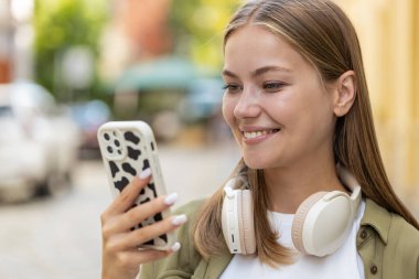 Akıllı telefon kullanarak mesajlar yazan güzel bir genç kadın. İnternetteki sosyal medya uygulamalarına bakarak dışarıda sohbet ediyor. Şehir caddesinde beyaz bir genç kız. Yaşam Tarzları
