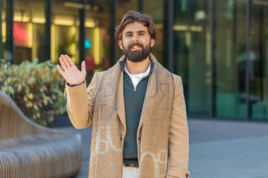 Neşeli Arap turist, kameraya gülümseyen, el sallayan, el sallayan merhaba, merhaba, merhaba, güle güle, misafirperver bir yüz ifadesiyle hoş geldiniz. Şehir merkezinde mutlu bir adam