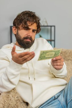 Zavallı Hintli Arap 'ın portresi bir dolar banknotunu gösteren yetersiz miktarda para yüzünden üzgün. Finansal kriz. İflas. Yoksulluk. Evdeki kanepede oturan üzgün İspanyol adam..