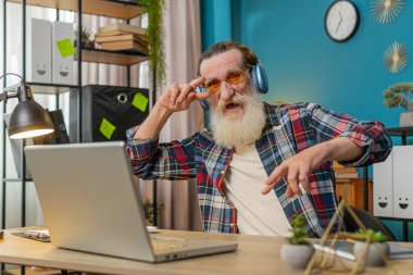 Memnuniyetle ofis masasında oturan yaşlı adam kablosuz kulaklıkla en sevilen enerjik disko müziğini dinliyor. Heyecanlı serbest çalışan dede dinleniyor, dizüstü bilgisayarla masa başında mola veriyor.