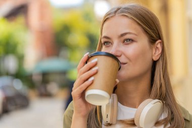 Kafkasyalı mutlu kadın sabah kahvesinin tadını çıkarıyor sıcak içecek ve gülümsüyor. Dinleniyorum, ara veriyorum. Şehir merkezi caddesinde yürüyen genç bir kız, gitmek için kahve içiyor. Dışarıdaki kasaba yaşam tarzları.
