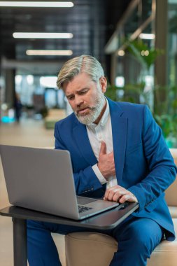 Diz üstü bilgisayar kullanan ve modern ofis lobisinde çalışırken kalp krizi geçirme riski taşıyan gerilimden muzdarip Kafkasyalı yetişkin işadamı. Takım elbiseli iş adamı.