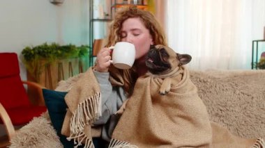 Beyaz saçlı genç bir kadın elinde sıcak ve sakin bir bardakla battaniye altında çay içiyor. Pug dog aynı battaniyenin altında huzur ve huzur dolu bir aile anını paylaşıyor..