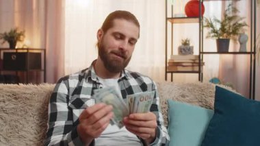Genç adam evdeki yeni kazanç maaşını kontrol ediyor, her para dolar banknotunu yavaş yavaş mutlu bir ifadeyle sayıyor. Kafkasyalı gülümseyen adam ortak finansal hedefler için fon sağlandığı için mutlu.