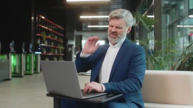 Kafkasyalı orta yaşlı işadamı ofis lobisinde dizüstü bilgisayarla çalışırken omurga kası ağrısından muzdarip. Çok çalışıyorum. Erkek girişimci, takım elbiseli adam masaj yaparak acıyı azaltmaya çalışıyor..