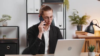 Mutlu Kafkas tarzı genç iş adamı müşteriyle telefon akıllı telefonuyla iletişim kuruyor, ofis masasında dizüstü bilgisayar ağı üzerinde çalışıyor. Takım elbiseli adam internetteki uzak mesafe işini temsil ediyor..