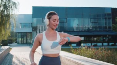 Atletik koşucu yetişkin kız akıllı cihaz fitness bileziğine bakar zamanı, kalp atışını, nabzı, koşuda SPO2 'yi kontrol eder. Şehir parkında müzik dinleyen genç bir kadın..