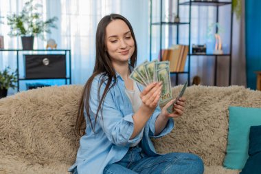 Evdeki genç kadın kanepeye oturup yığınla para sayarak zenginliği kutluyor. Kafkas kızı başarılı kişisel bütçeyi yönetiyor, mali kazancı tatmin ediyor.