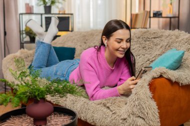 Evde, kulaklık takmış, kanepeye uzanmış genç bir kadın cep telefonuyla sosyal medya yayınını rastgele kaydırıyor. Kafkasyalı kız dinleniyor, çevrimiçi içerikten, müzikten, eğlenceden ve boş zamanlardan keyif alıyor..