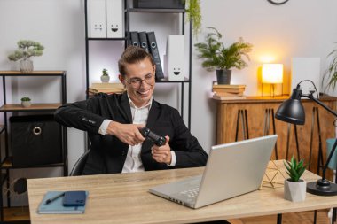 Kafkasyalı genç iş adamı laptopta video oyunu oynuyor, boş zamanlarını ofis masasında geçiriyor. Mola sırasında joystick kontrolörüyle video oyunu oynayan mutlu stil sahibi serbest yazar..