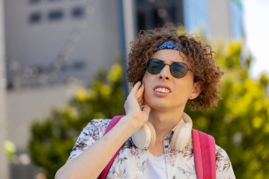 Şehir caddesinde diş ağrısından muzdarip beyaz bir genç turist. Kıvırcık saçlı ve sırt çantalı üzgün erkek elini yanağının yakınında tutuyor, hassas noktasına masaj yapıyor, acı hissediyor. Diş tedavisine ihtiyacı var.