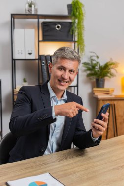 Akıllı telefon uygulamasını kullanarak mobil ekran uygulamasını gösteren kendine güvenen genç bir iş adamı. Ofiste çalışan uzaktan kumandalı bir iş. Kameraya bakan serbest çalışan yakışıklı bir adam. Reklamcılık