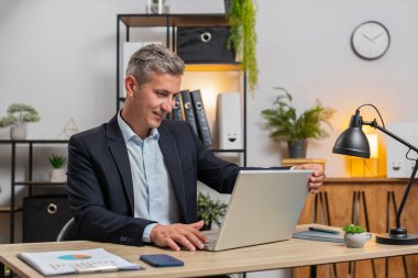 Resmi takım elbiseli genç, gri saçlı işadamı dizüstü bilgisayarı açıyor mesajlar gönderiyor, filmler izliyor, online alışverişler yapıyor. Modern ofis çalışma alanında netbook kullanan beyaz bir adam..