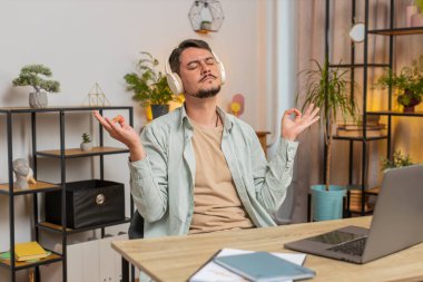 Sakin ol, sakin ol. Müzik dinleyen adam derin nefes alır, gözleri kapalı konsantre düşüncelerle meditasyon yapar, huzurlu bir zihin. Genç serbest çalışan biri ofis masasının çalışma yerinde oturuyor. Yaşam biçimi.
