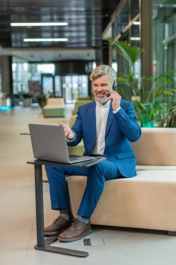 Kafkas işadamı kulaklık takıyor, çağrı merkezi ya da destek operatörü yardım hattı kullanıyor, ofis lobisinde müşteri ya da iş arkadaşı ile iletişim desteği ile konuşuyor. Takım elbiseli adam oteldeki koltukta oturuyor..