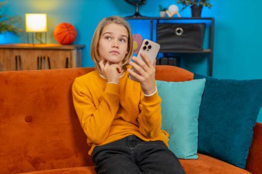 Beyaz çocuk evde akıllı telefondan bulmaca çözme girişiminde bulunuyor. Düşünceli ifade çözüm bulma seviyesini yükseltiyor, koltukta oturup memnuniyet gösteriyor.