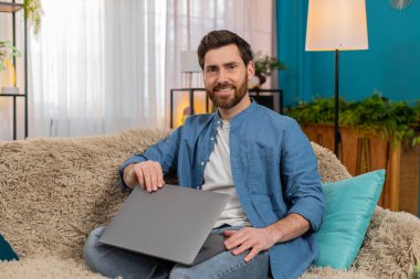 Evdeki genç adam işini bitirdikten sonra bilgisayarını kapatırken memnuniyetle gülümsüyor. Kanepede oturan beyaz adam kendini başarılı, rahatlamış ve projelerini tamamlamaktan mutlu hissediyor.