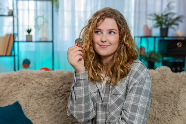 Altın Bitcoin BTC 'yi elinde tutan genç bir kadın. Kripto yatırım seçeneklerini incelikle analiz ediyor. Kanepede oturan beyaz saçlı kız finansal stratejinin dijital para birimi planladığını düşünüyor.