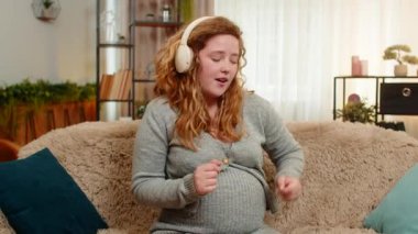 Hamile ve mutlu bir kadın evde kulaklıkla müzik dinliyor, karnına hafifçe dokunuyor, dikkatli adımlarla ve pozitif ruh haliyle dans ediyor. Kız ritimden hoşlanıyor, aşkı, bağlantıyı ve mutluluğu hissediyor..