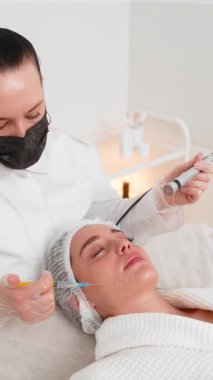 Enjeksiyonsuz mezoterapi ya da elektroporasyon. Güzellik doktoru, kadın müşteriyi güzellik kliniğinde terapiye götürür. Kız cilt bakımı anti-yaş spa prosedürü. Estetik kozmetoloji. Dikey video