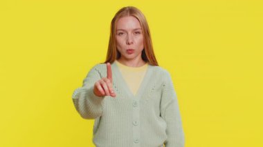 Mutsuz bir kadın nahoş berbat bir fikre tepki veriyor, kötü kaliteden memnun değil, el sallıyor, başını sallıyor hayır, reddet fikri, evlenme teklifini sevme. Sarı arka planda izole edilmiş genç bir kız.