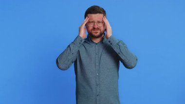Keyifsiz, orta yaşlı, gözlüklü, baş ağrısı problemini tedavi etmek için şakak ovalayan orta yaşlı beyaz bir adam migren stresinden muzdarip. Acı içinde kıvranan bir adam, mavi arka planda yüksek tansiyon.