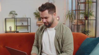 Kahverengi saçlı, beyaz bir adam oturma odasındaki işi bittikten sonra bilgisayarını kapatıyor. Mutlu genç adam serbest çalışıyor. Evinde uzaktan kumanda işinde çalışıyor. Bilgisayarda E-öğrenme, internette gezinme