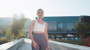 Aktif giyimli mutlu beyaz kadın portresi kameraya bakıyor. Güzel gülümseyen sporcu kadın kolları çapraz kollarıyla şehir parkında sağlıklı yaşam tarzı egzersizi yapıyor.