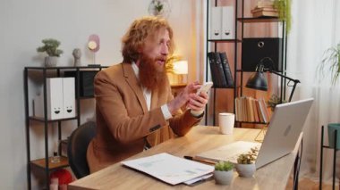 Kendine güvenen kızıl saçlı işadamı internet üzerinden akıllı telefon uygulaması kullanarak konuşuyor. Onaylıyor, uzaktan kumandayla çalışıyor. Kameraya bakan serbest çalışan bir adam. Reklamcılık