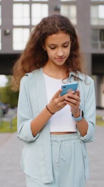 Gülümseyen ergen çocuk akıllı telefon kullanıyor mesajlar yazıyor sohbet mesajları yazıyor mobil ekranlı sosyal medya uygulaması. Kız turist ellerinde telefonla şehir sokaklarında yürüyor.