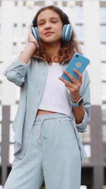 Kablosuz kulaklıklı, neşeli, çocukluk çağındaki çocuk dışarıda dans eden enerjik disko rock 'n roll müziği dinliyor. Şehir caddesinde yürüyen genç bir kız. Dikey