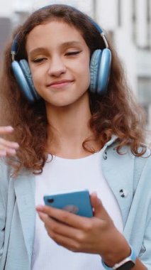 Kablosuz kulaklıklı, neşeli, çocukluk çağındaki çocuk dışarıda dans eden enerjik disko rock 'n roll müziği dinliyor. Kentsel Avrupa şehir caddesinde yürüyen bir kız. Dikey