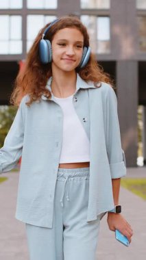 Kablosuz kulaklıklı, neşeli, çocukluk çağındaki çocuk dışarıda dans eden enerjik disko rock 'n roll müziği dinliyor. Şehir sokaklarında yürüyen bir kız. Dikey